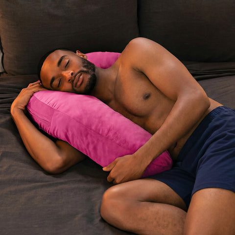 Man in navy sleep shorts resting on the pink Lune Snuggle Pillow